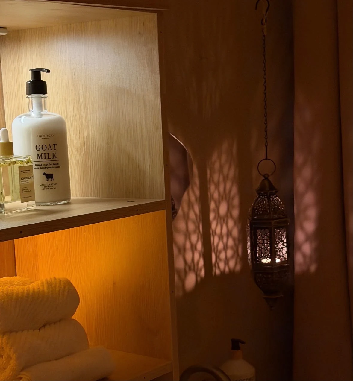 Warmly lit shelf with oils, towels, and a hanging lantern